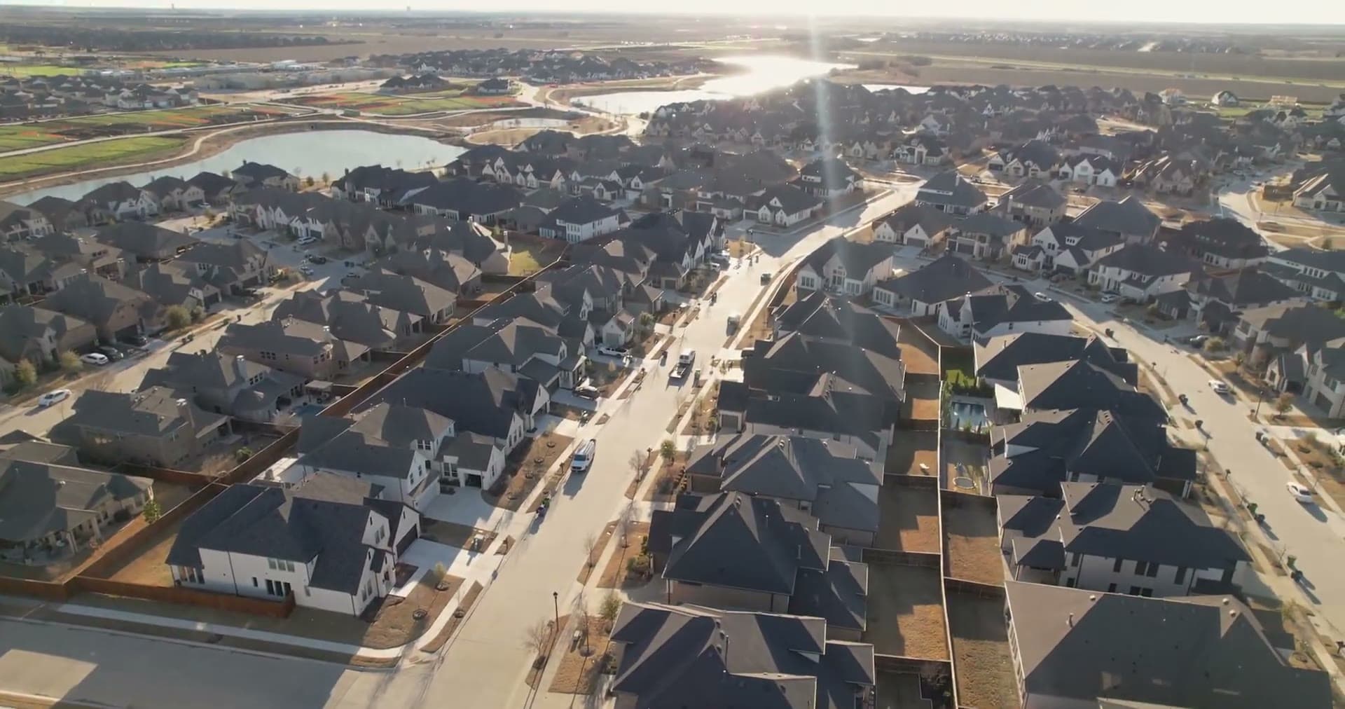Golden hour aerial over a Texas community with rooftop solar and lakes.